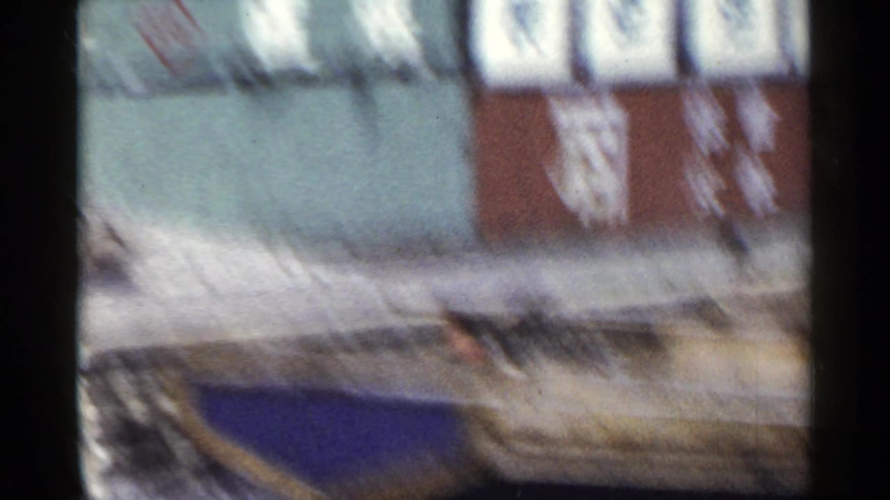 1953 Japan home-movie frame from a moving train, showing weathered walls with large Japanese characters and a low stone or curb edge.