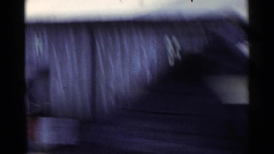 1953 Japan 8mm frame with a blurred corrugated-roof building or shed passing close to the camera.