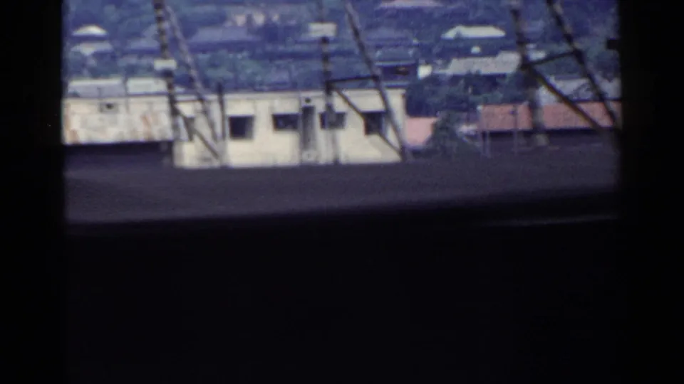 1953 Japan home-movie view of low rural buildings, rooftops, bare trees, and utility lines seen in passing.