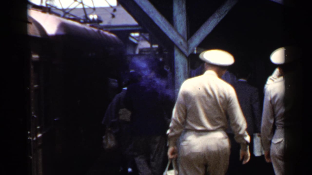 Passengers and uniformed men walk beside a train under a wooden station canopy.