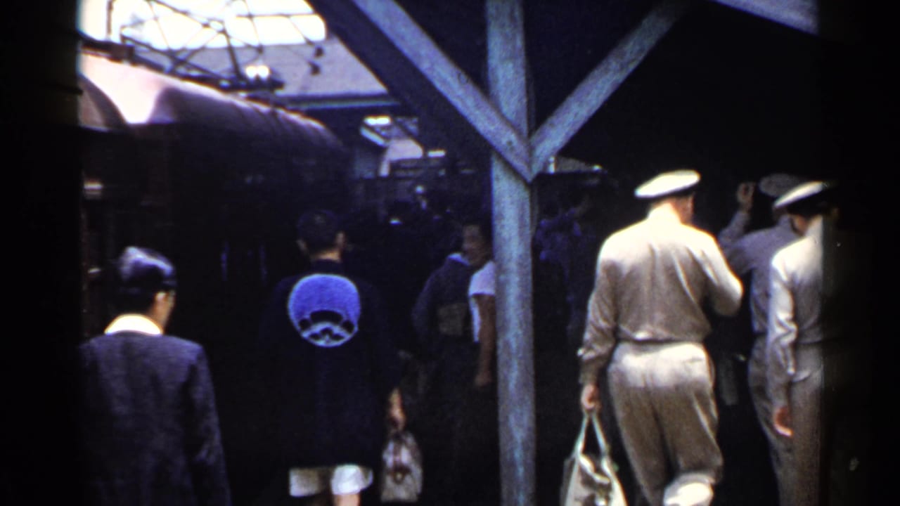 Crowd moves near a train with uniformed men and civilians carrying bags.