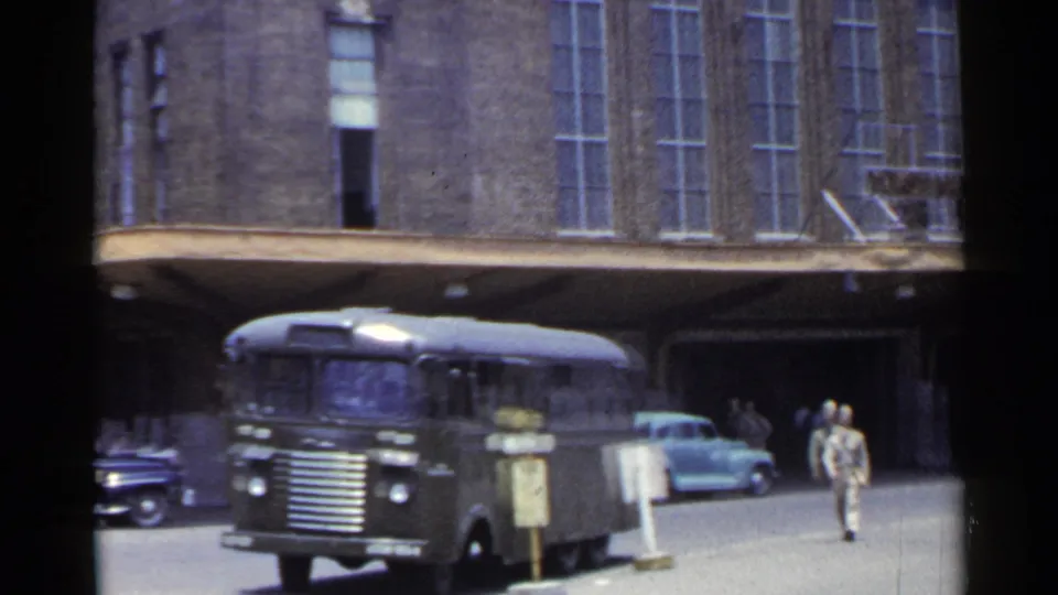 1953 Japan 8mm frame with a dark bus in the foreground, pedestrians near the terminal entrance, and mid-century cars behind.