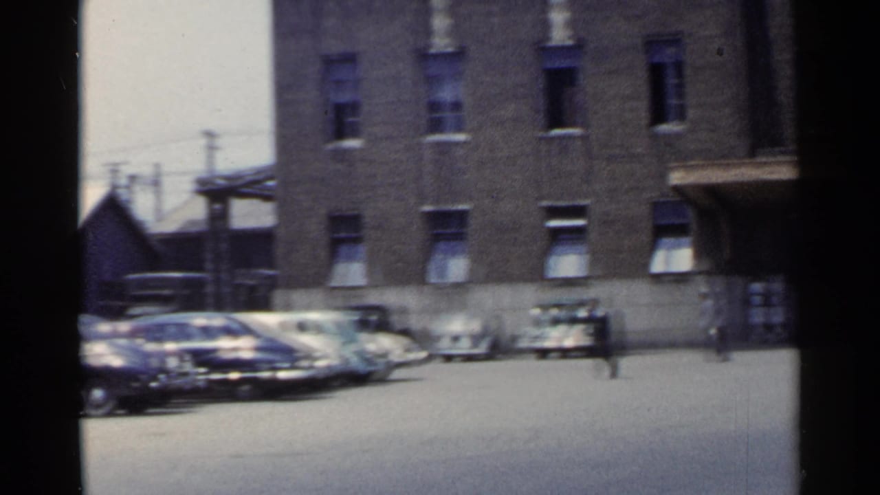 Parked cars lined beside a brick building in a bright paved lot.