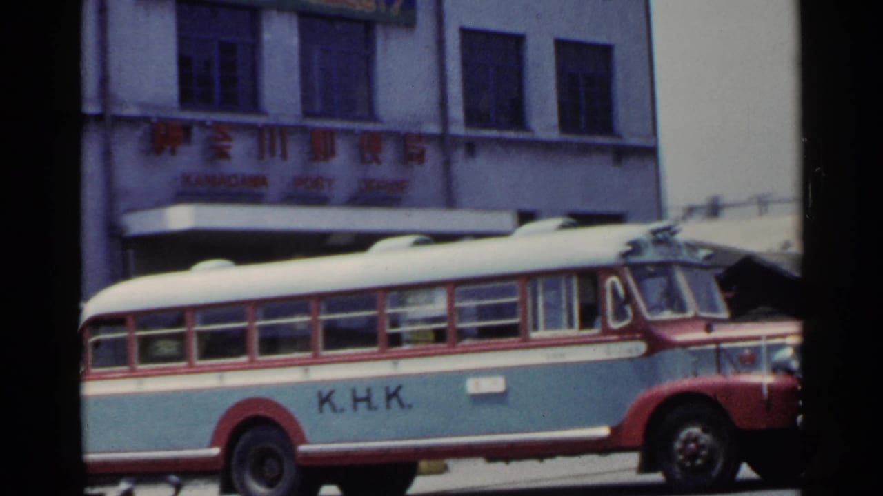 K.H.K. bus passing in front of a building with Japanese signage.