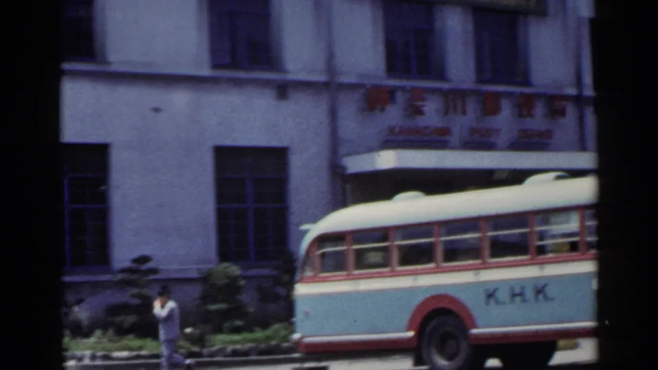 1953 Japan street frame with part of a K.H.K. bus, a pedestrian, and a civic-looking building facade.