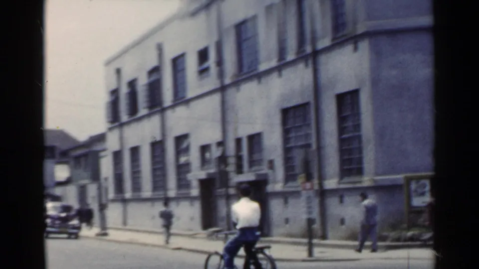 1953 Japan street view with a cyclist in the foreground, pedestrians, street posts, and a long building facade.
