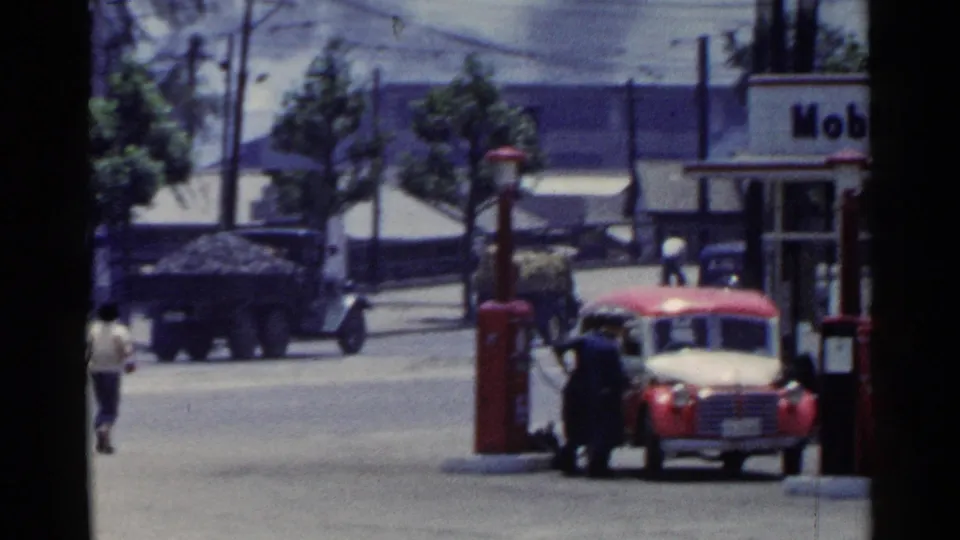 1953 Japan Mobilgas station scene with a red and white car, fuel pumps, attendants, pedestrians, and street frontage.