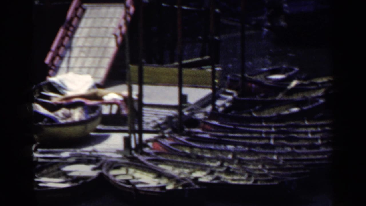 1953 Japan home-movie frame showing moored small boats, dock edges, and water seen through a dark partial obstruction.