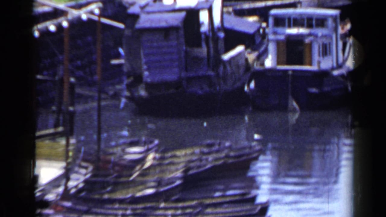 1953 Japan waterfront view with small cabin boats and dock structures reflected in a narrow stretch of water.
