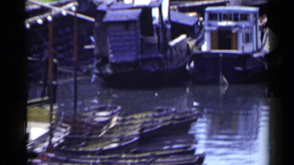 1953 Japan waterfront view with small cabin boats and dock structures reflected in a narrow stretch of water.