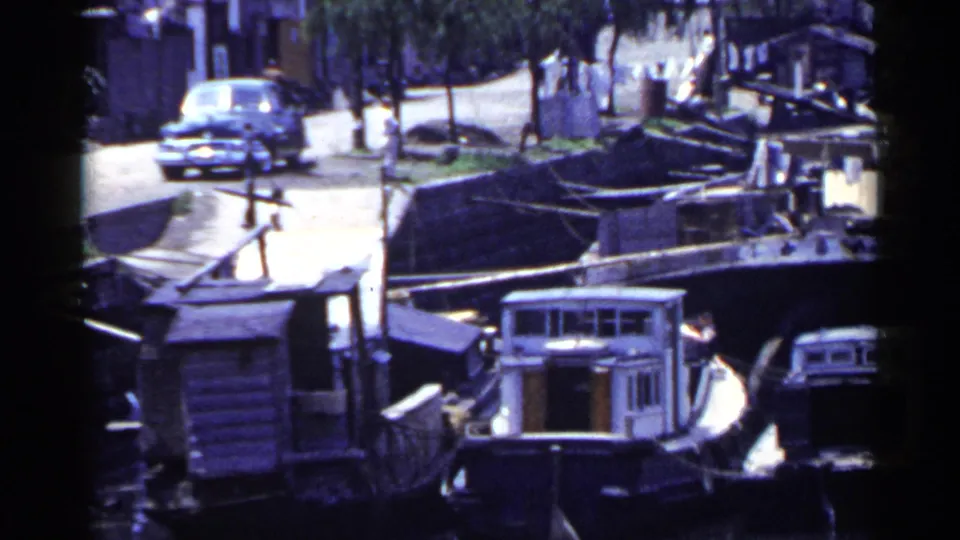 1953 Japan marina scene with moored boats, a road, a vintage car, and small pedestrians visible near the waterfront.