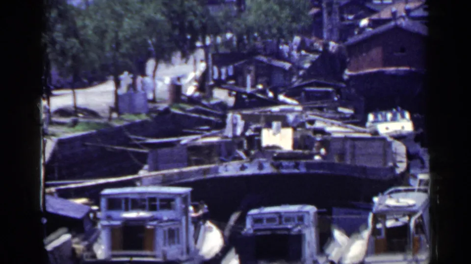 1953 Japan home-movie view across moored marina boats toward road traffic, trees, and distant pedestrians.