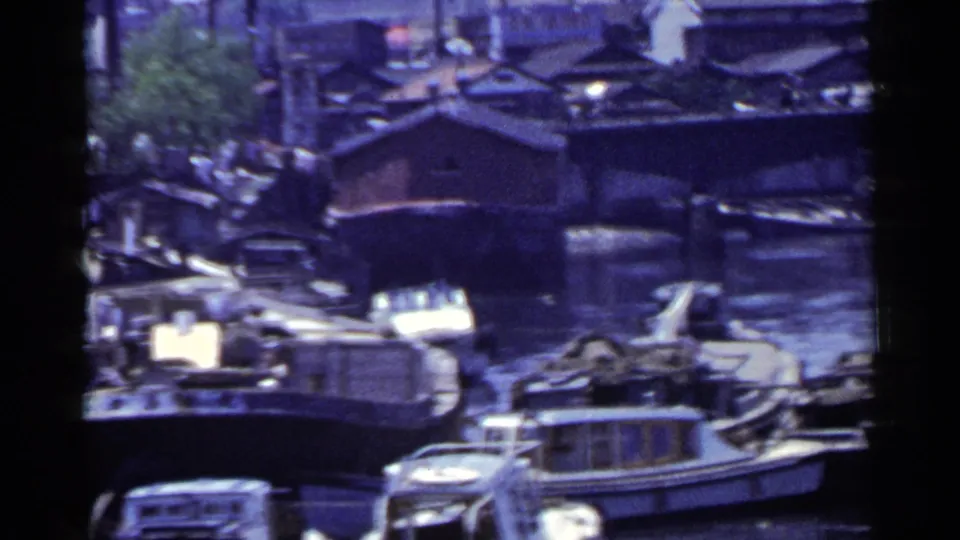 1953 Japan home-movie frame with compact boats, cabin boats, and dark wooden structures along a busy canal.