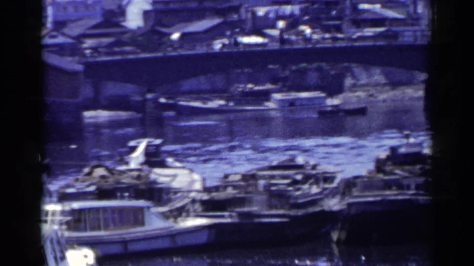 1953 Japan 8mm view of a bridge crossing a canal, with small boats and waterfront buildings visible through aged film color.