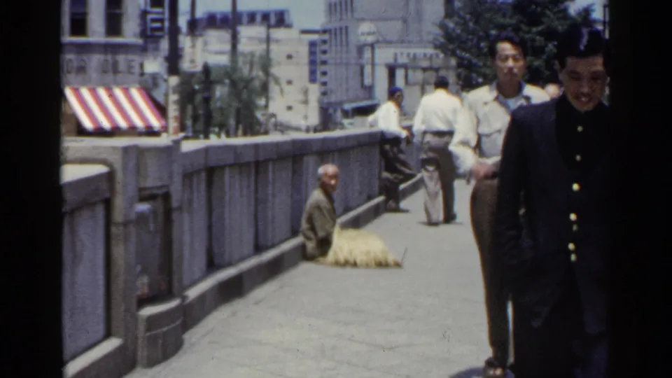 1953 Japan urban bridge or raised sidewalk with a seated man in the background and pedestrians passing nearby.