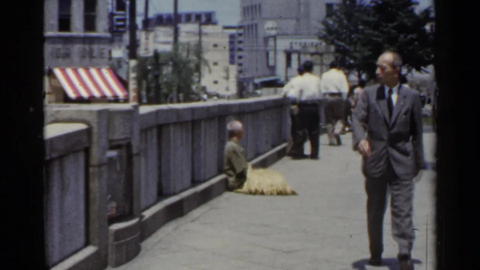 A suited pedestrian walks through a 1953 Japan bridge walkway scene while a seated person and straw-like bundle remain by the stone railing.