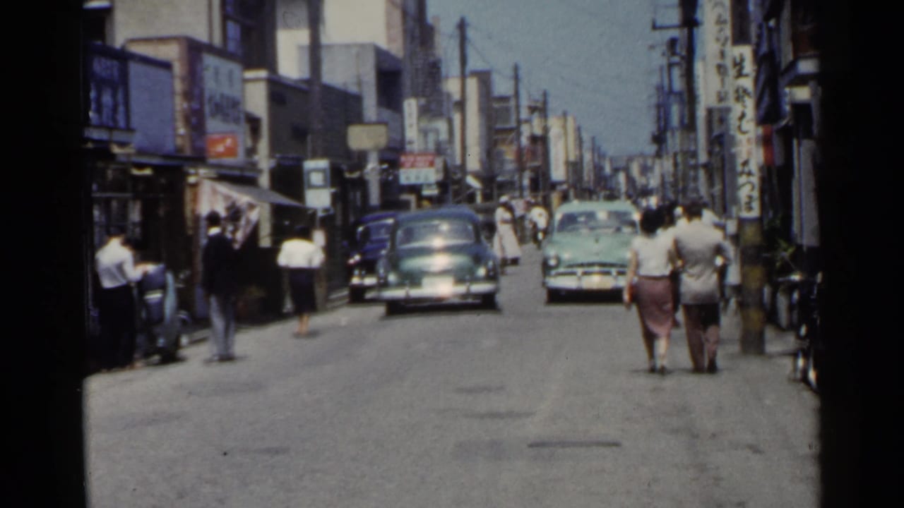 Street scene with cars ahead, pedestrians on the right, storefront signs, and utility poles.