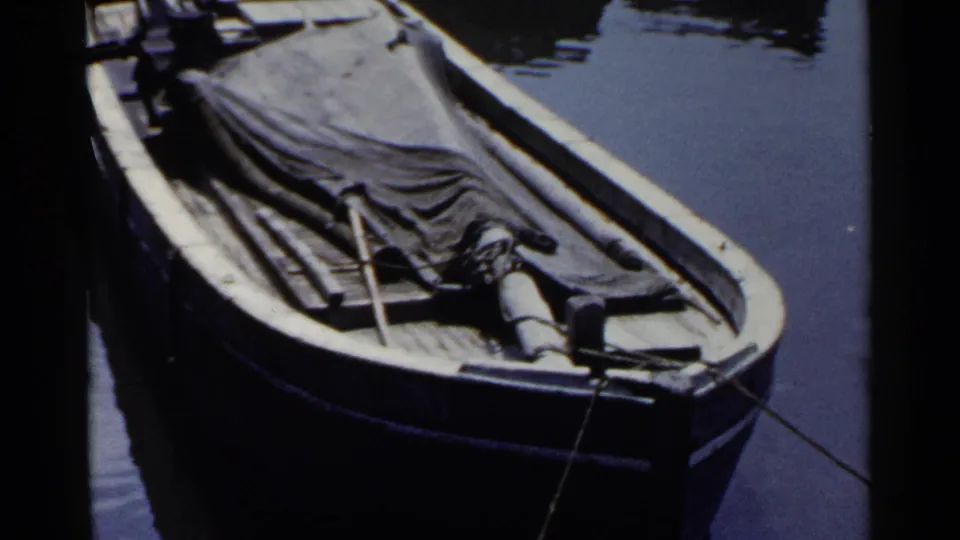 1953 Japan home-movie frame showing a covered wooden boat tied along a calm canal or waterway.