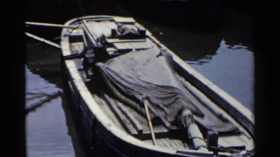 1953 Japan home-movie frame of a tarped wooden boat resting near a dock in still water, with deck details visible.