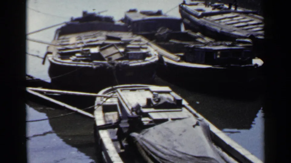 1953 Japan waterfront frame with small wooden boats tied side by side, their decks and tarps visible in soft 8mm color.