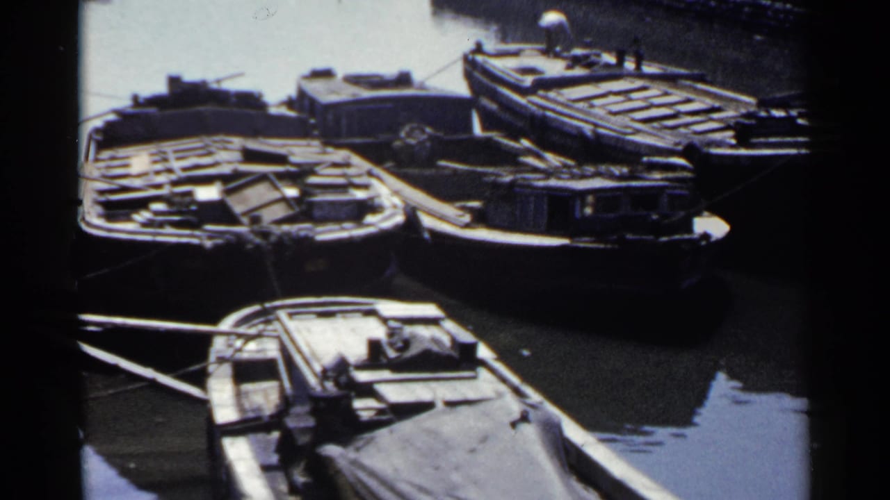 1953 Japan harbor view with wooden barges and small moored boats beside calm canal water.