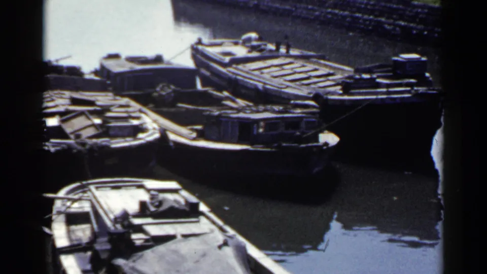 Moored wooden barges and compact boats appear along a stone-lined Japanese harbor canal in 1953 footage.