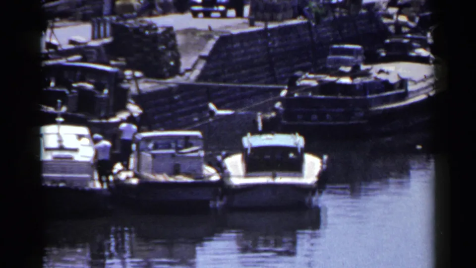 Japanese harbor landing with moored small boats, barges, stone steps, and a few distant people near the water.