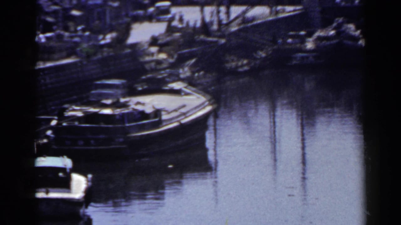Motorboat and larger vessel docked beside a still canal with shoreline structures behind.