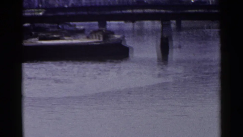 1953 Japan canal frame with bridge supports reflected in calm water and part of a moored boat along the embankment.