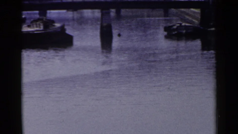 1953 Japan harbor view with calm water, dark structural beams, small boats, and stone-lined waterfront edges.