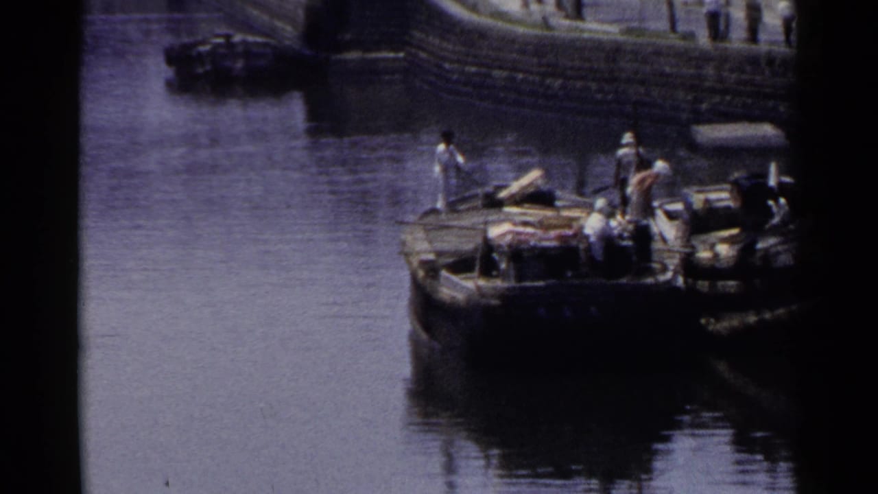 Moored wooden boat with people aboard beside a stone-lined harbor wall.