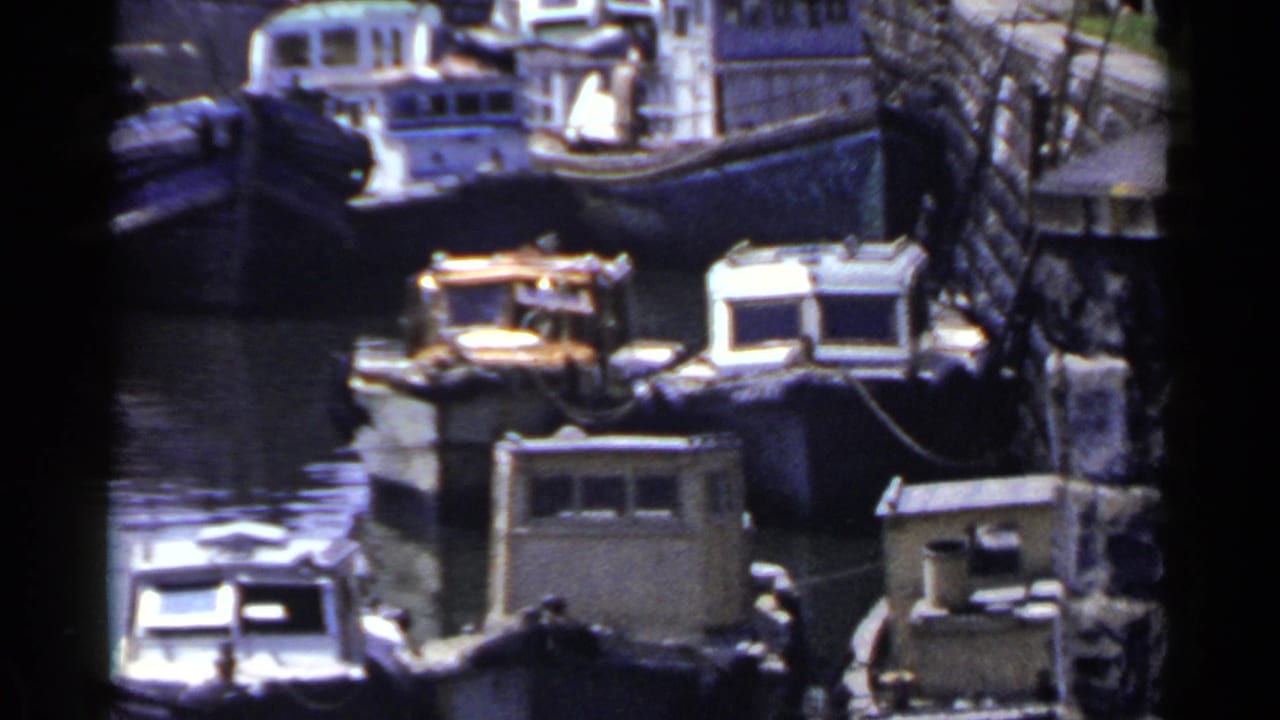 Clustered small boats and cabin roofs beside a canal wall with water in the foreground.