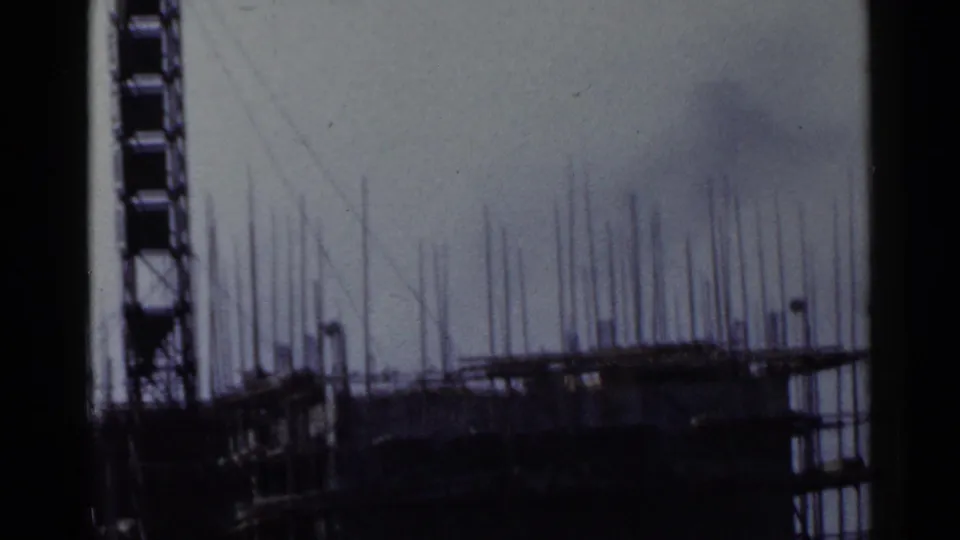 1953 Japan 8mm frame showing a tall scaffolded construction structure with vertical rods and dark film edge borders.