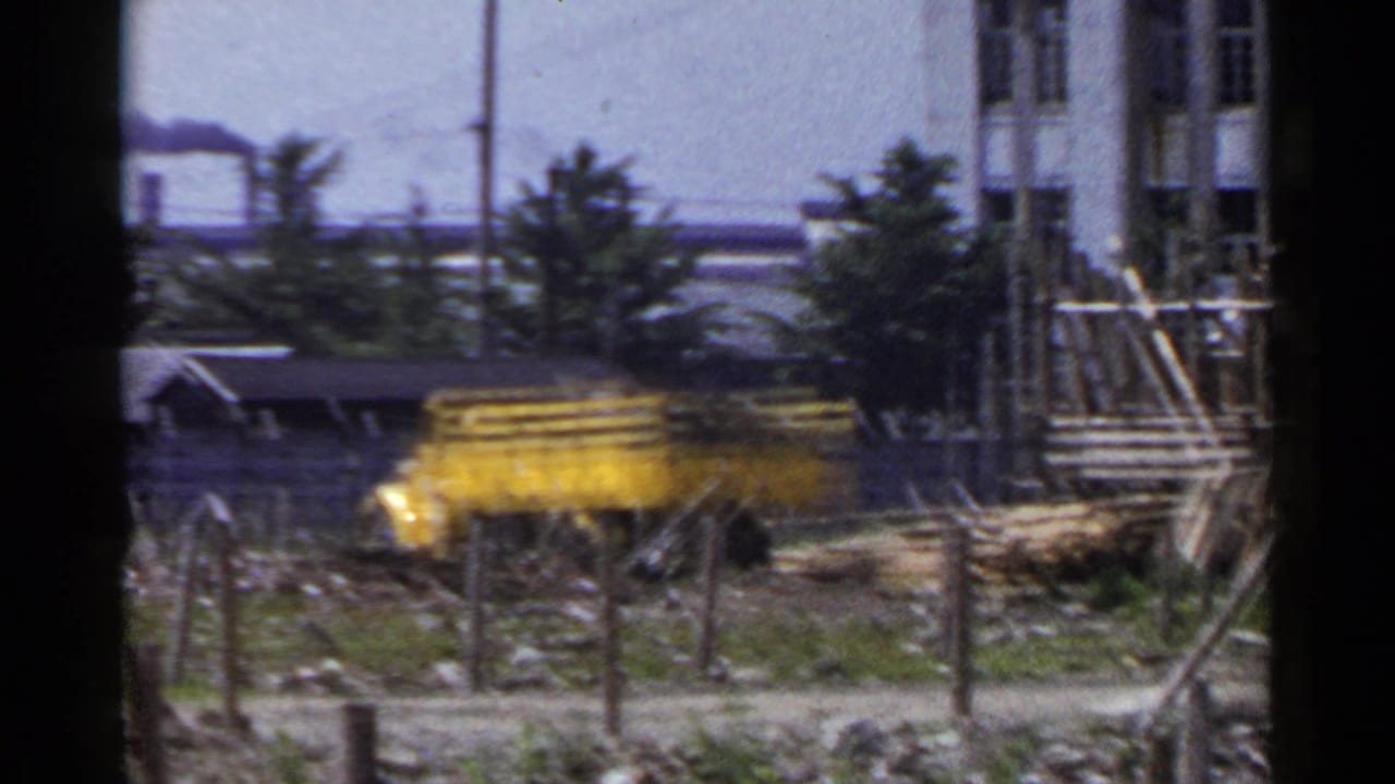 Yellow dump truck beside construction debris with factory smoke and utility poles in the background.
