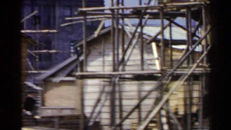 1953 Japan 8mm frame focused on wooden scaffolding and a small light-colored structure at a construction site.