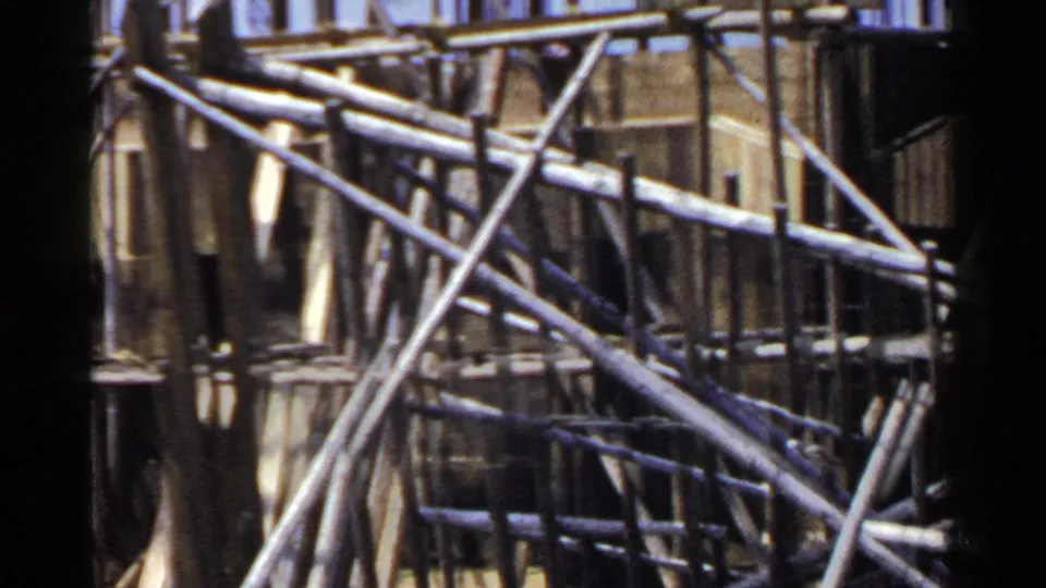 1953 Japan frame with overlapping bamboo scaffold poles, lashings, and shadowed wooden surfaces behind them.