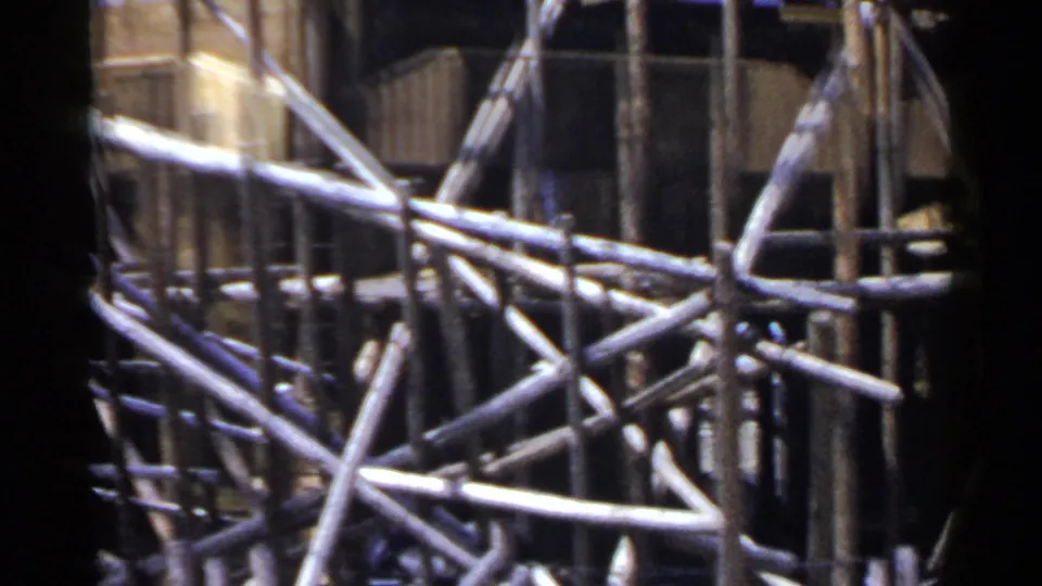 1953 Japan home-movie frame showing angled bamboo scaffold braces in front of dark wooden building sections.
