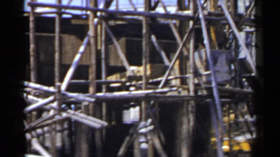 1953 Japan frame showing bamboo scaffold rails, diagonal supports, and partial wooden building surfaces in warm light.
