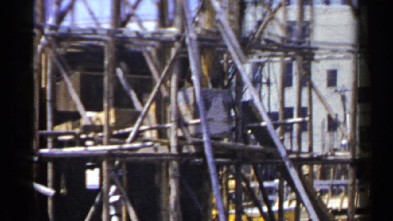 Wooden scaffolding and planks around a pale multi-story building.
