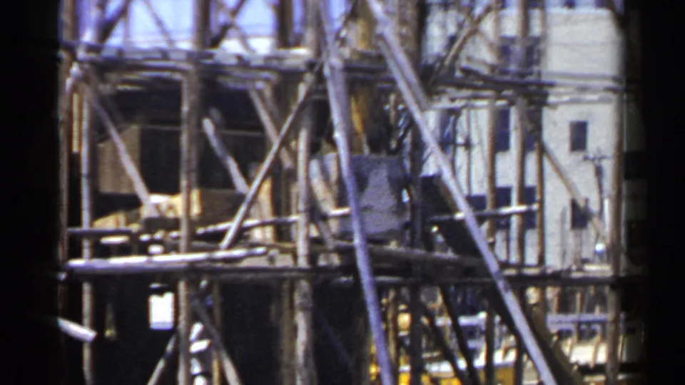 1953 Japan 8mm frame showing wooden scaffolding, cross braces, and planks against a pale building facade.