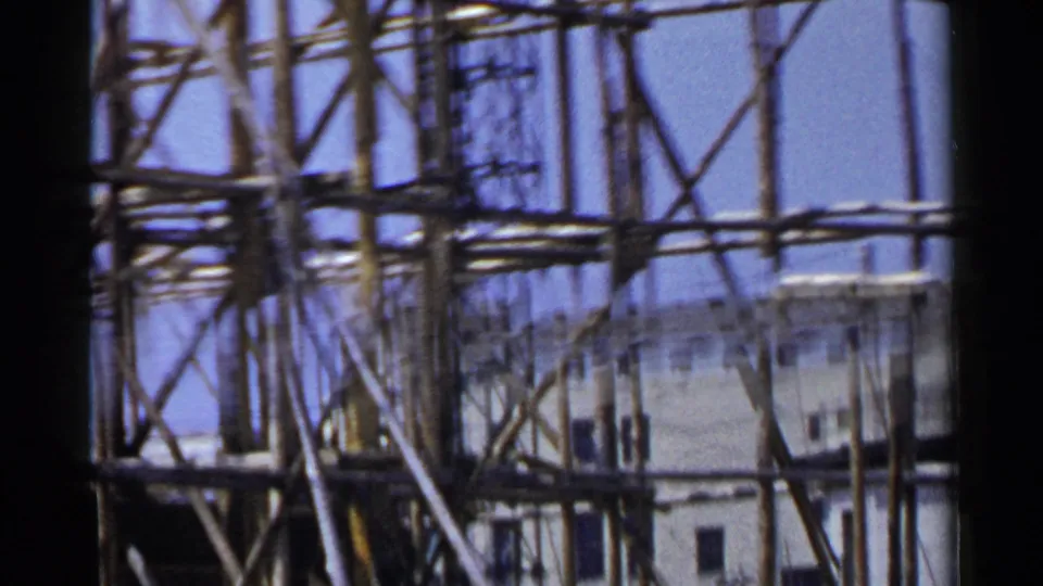 1953 Japan 8mm frame showing wooden construction scaffolding rising above a building edge under clear blue sky.