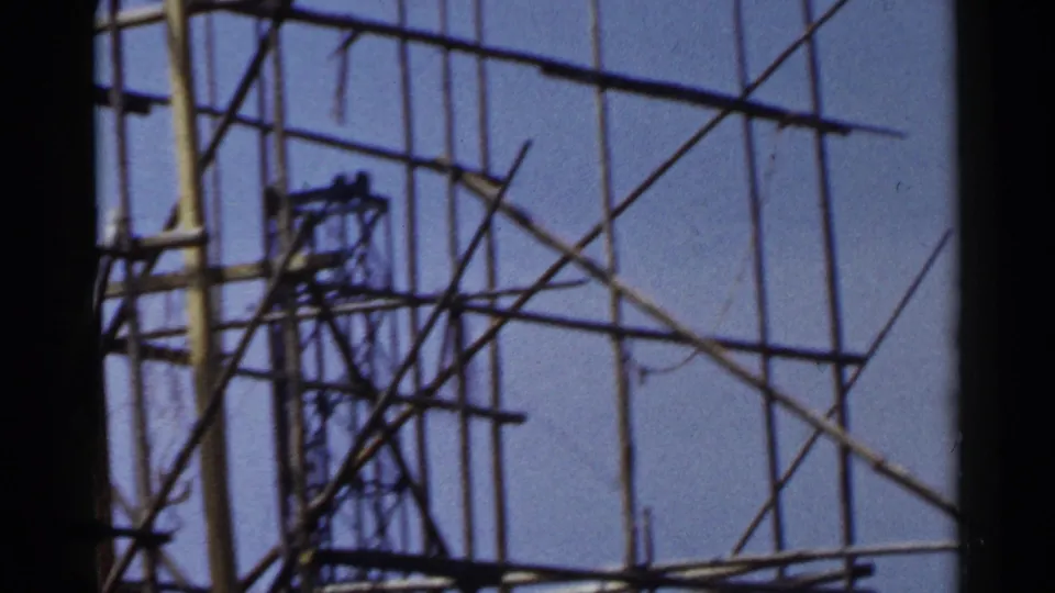 1953 Japan 8mm frame with a sparse wooden scaffold lattice and diagonal braces set against bright blue sky.