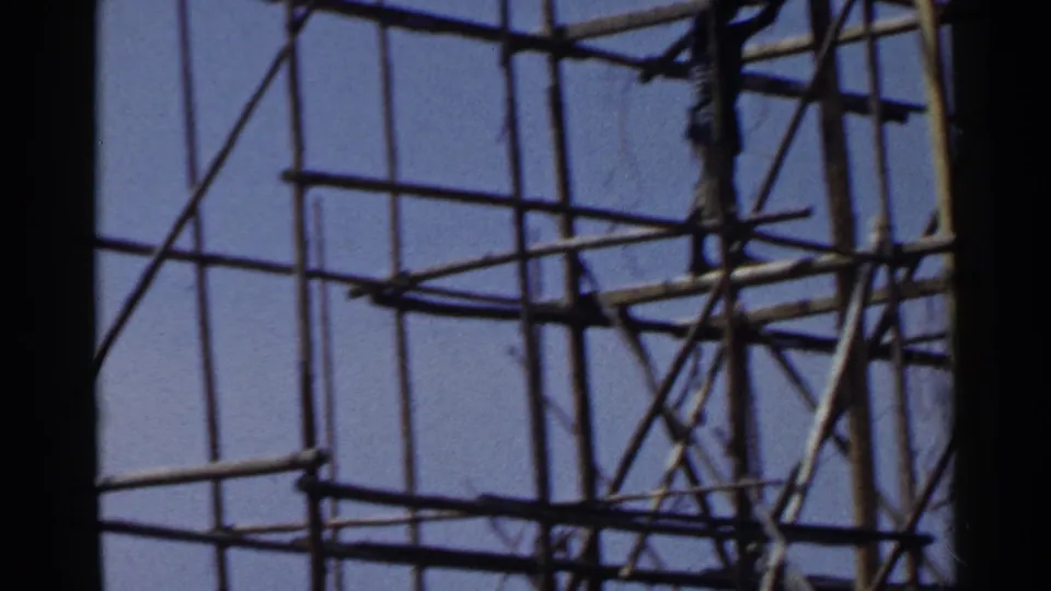 1953 Japan home-movie frame with dense scaffolding, angled braces, and a partially visible worker near the upper frame.