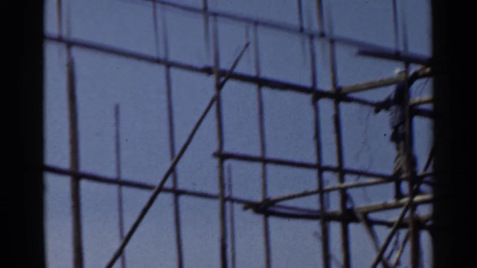 1953 Japan frame showing bamboo-like scaffolding and a distant construction worker partly cropped by the right edge.