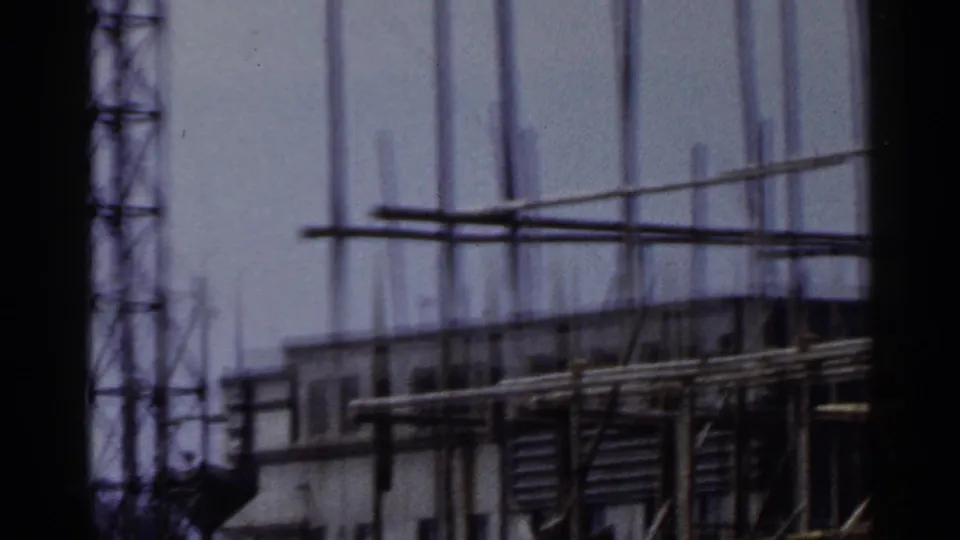1953 Japan construction footage showing scaffolding and part of an unfinished multi-floor structure in soft focus.