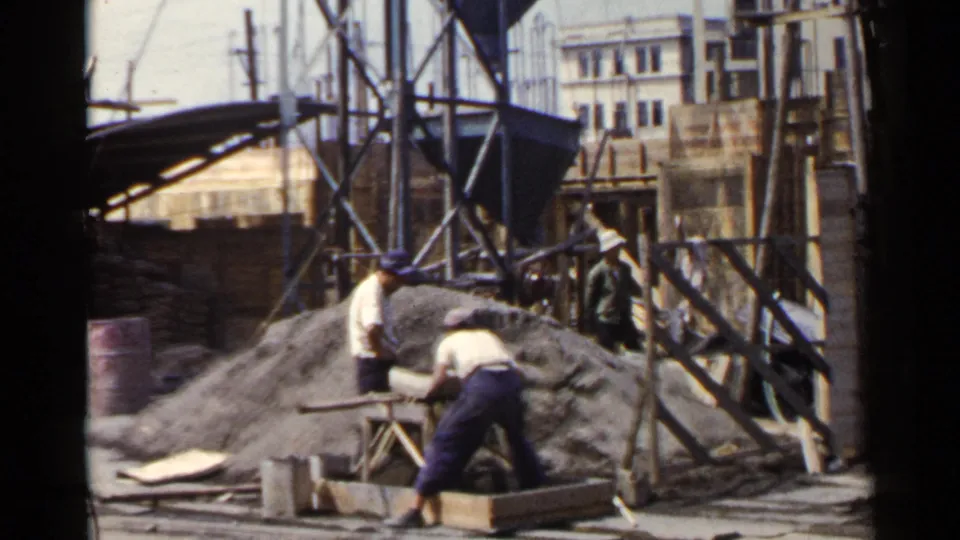 In this Japan 1953 construction view, one worker bends over a foreground form while another stands near the aggregate pile and temporary supports.