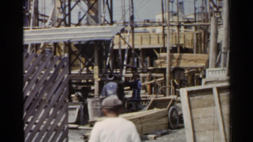 1953 Japan frame with a foreground figure watching or passing a construction site where workers and scaffolding are visible.