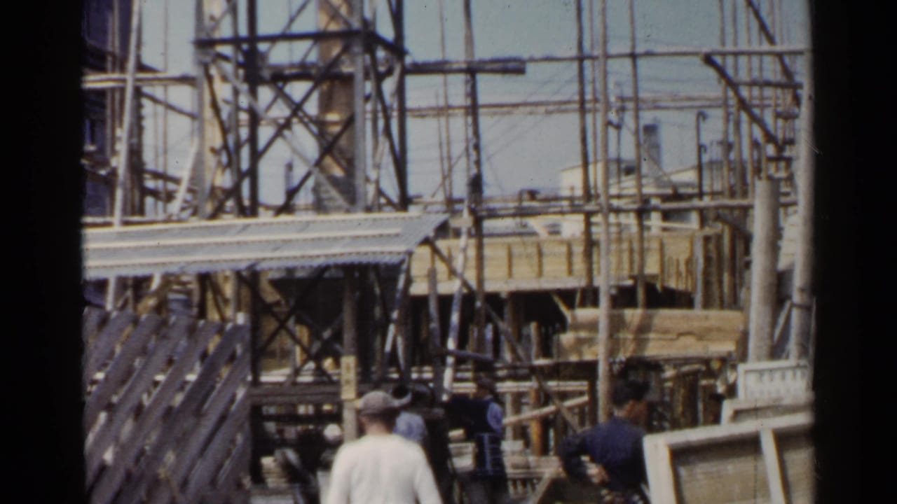 1953 Japan construction view with workers in caps, timber boards, scaffold poles, and a partially built structure.