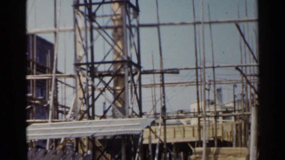 1953 Japan frame showing scaffold towers, wooden platforms, upright poles, and portions of a construction site.