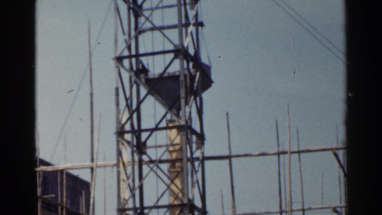 Steel lattice tower with platform sections and guy wires against a pale sky.